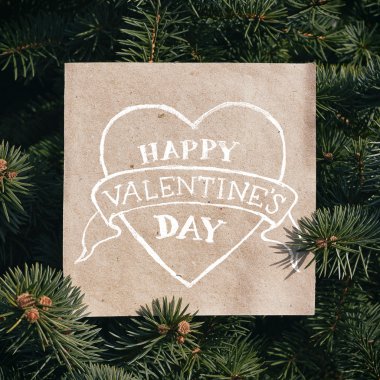 Eco craft paper card on pine tree background. Holiday square poatcard template. Heart shape drawn, happy valentine's day lettering, text.