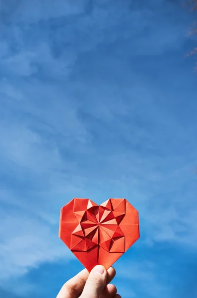 Rosso piegato origami cuore di carta in mano su sfondo cielo blu. Modello di cartolina Hippster. Spazio per copia, lettering, testo . — Foto Stock