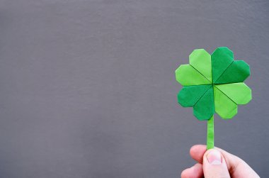 Kağıt origami Yeşil yonca gri duvar arka planda tutan el. Kopya yazı, metin, alan. St. Patrick'ın gün kartpostal şablonu.