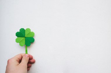 Hand holding paper origami green shamrock on white wall background. Space for copy, lettering, text. St. Patrick's day postcard tempalte.