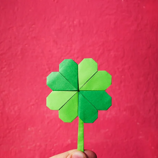 Hand die papier origami groene klaver op roze muur achtergrond. Ruimte voor kopie, belettering, tekst. St. Patrick de dag briefkaart tempalte. — Stockfoto