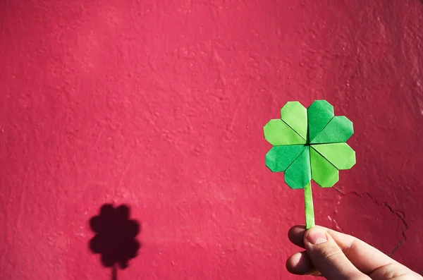 Kağıt origami Yeşil yonca pembe duvar arka planda tutan el. Kopya yazı, metin, alan. St. Patrick'ın gün kartpostal şablonu. — Stok fotoğraf