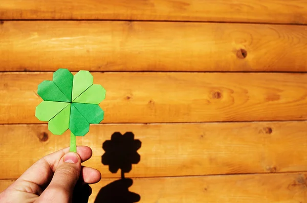 Hand hält Papier Origami grünen Shamrock auf Holz Wand Hintergrund. Raum für Kopie, Schrift, Text. st. patrick 's day postcard tempalte. — Stockfoto