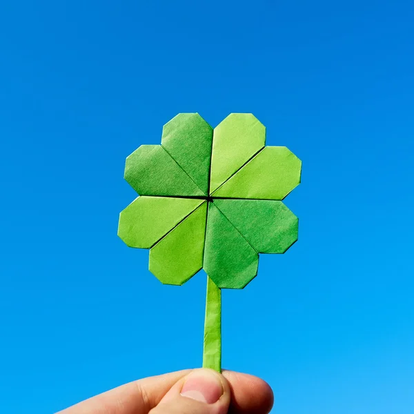 Mano sosteniendo papel verde origami doblado trébol sobre fondo azul cielo. Tiempo soleado al aire libre . —  Fotos de Stock