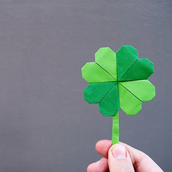 Kağıt origami Yeşil yonca gri duvar arka planda tutan el. Kopya yazı, metin, alan. St. Patrick'ın gün kartpostal şablonu. — Stok fotoğraf