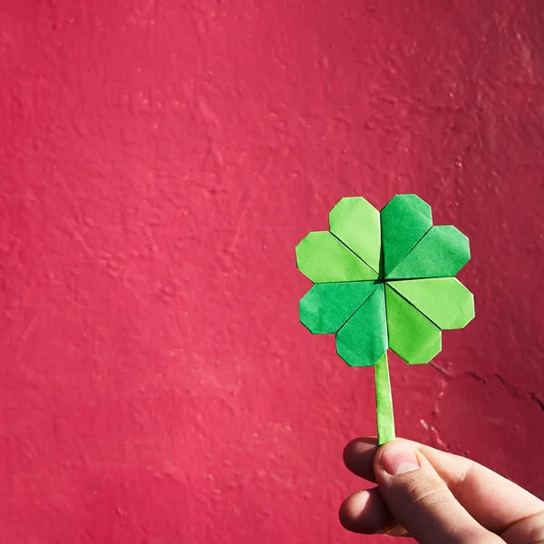 Mão segurando papel origami verde shamrock no fundo da parede rosa. Espaço para cópia, letras, texto. Dia de São Patrício cartão postal tempalte . — Fotografia de Stock