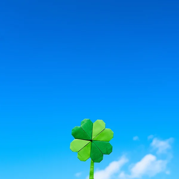 Green paper origami folded shamrock on blue sky background. Sunny weather outdoors. Sapce for text, lettering, copy. — Stock Fotó
