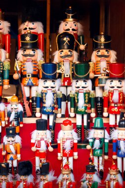 Renkli ahşap fındıkkıran heykelcikleri Noel pazarındaki şenlikli kırmızı arka planda sergileniyor. Tatil tasarımları ve mevsimlik temalar için geleneksel el yapımı dekor ideali.