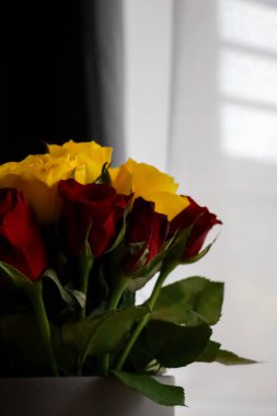 Yeşil yapraklı kırmızı ve sarı güllerden oluşan buketi kapat. Yumuşak doğal pencere ışığında, tarafsız arkaplanda. Romantik ve şenlikli durumlar için zarif bir çiçek aranjmanı..