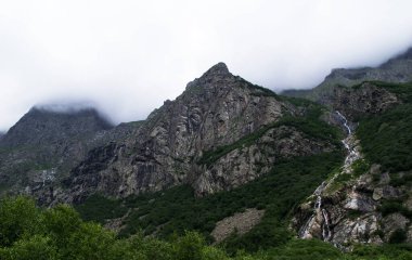 Midagrabindon şelaleleri vadide. Yazın Kuzey Kafkasya 'da dağlar. Bulutlarda dağın tepeleri.