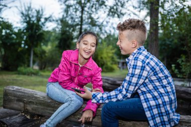 Gülen çocuklar akıllı telefonu birlikte otururken, mutlu erkek kardeş cep telefonu tutarken gülümseyen kız ve erkek kardeşle mobil uygulamanın keyfini çıkarırken, kız ve erkek çocuk küçük bir aletle mobil oyun oynarken eğlenirken..