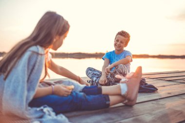 Gün batımında gölün kenarında oturan iki küçük sevimli arkadaş, erkek ve kız konuşuyor. Seçici odak.