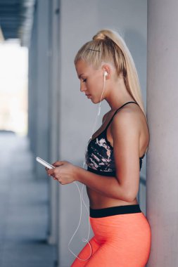 Spor giyim sektöründe cep telefonu kullanan ve müzik dinleyen bir kadının portresi.