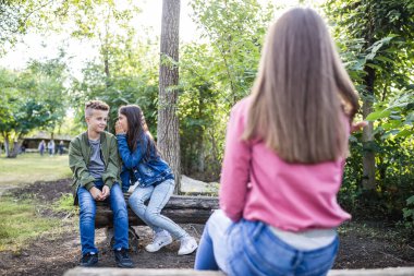 Oğlan ve kız, yanlarında oturan bir kız hakkında dedikodu yapıyorlar. Kız erkek kulağına bir şeyler fısıldıyor ve birlikte eğleniyorlar. Seçici odak.