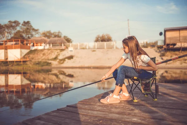 一个白人小女孩坐在一个木制码头上 手里拿着钓竿 在阳光明媚的夏日 可爱的孩子在湖上钓鱼 有选择的重点 — 图库照片