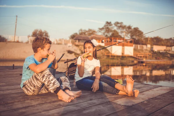 两个年轻可爱的小朋友 男孩和女孩吃三明治 在阳光明媚的夏日在湖面上聊天和钓鱼 孩子们在一起玩 玩得很开心 有选择的重点 — 图库照片