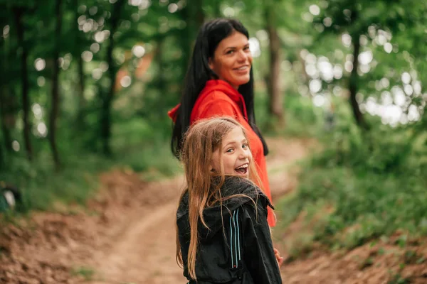 美丽的年轻母亲和她微笑的女儿手牵着手穿过森林 他们在镜头里看 有选择的重点 — 图库照片