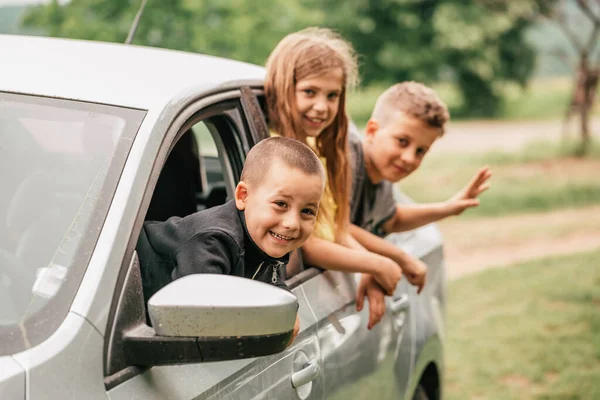 Drie Gelukkige Kinderen Zwaaien Met Hun Handen Door Hun Autoruiten — Stockfoto