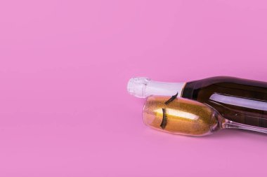 Şampanya şişesi, bir bardak altın parıltı ve pastel pembe arka planda kirpiklerle yaratıcı minimum konsept. Soyut kutlama ve parti daveti konsepti.