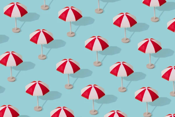 Creative idea, a pattern of colorful umbrellas on a light blue background. Minimal summer vacation concept.