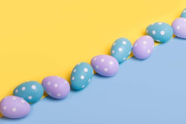 Sarı ve mavi arkaplanı aydınlatmak için çapraz dizilmiş renkli yumurtalardan oluşan yaratıcı Paskalya düzeni. Asgari paskalya konsepti. Metin için kopyalama alanı olan Paskalya kartı.