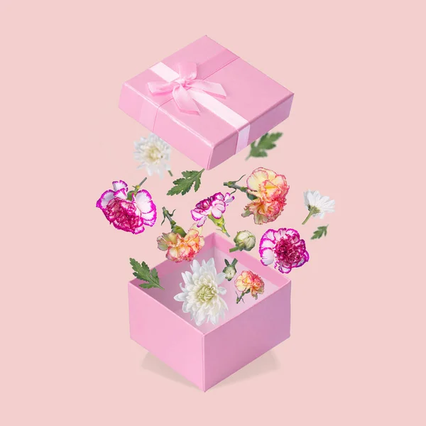 Luxurious Gift box with flying coloful flowers and leaves on a light pink background. Minimal spring or summer concept. A modern fun concept of gifts, wedding, anniversary and love.