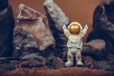 Astronot kayalık dağda dururken kollarını kaldırıyor. Uzay adamı beyaz uzay giysisi ve miğfer giyiyor. Kozmonotlar, uzay yolculuğu, özgürlük ve kazanma kavramı.