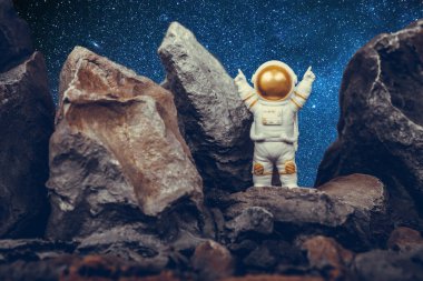 Kayalık dağda dururken kollarını kaldıran tatmin olmuş astronot. Uzay adamı beyaz uzay giysisi ve miğfer giyiyor. Kozmonotlar, uzay yolculuğu, özgürlük ve kazanma kavramı.
