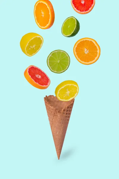 Minimal idea with ice cream cone and fresh orange, lime, lemon and grapefruit sliced, on pastel blue background. Minimal summer fruit concept.Vitamins, healthy diet concept. Mix of citrus fruit floating in the air. Creative concept with flying fruits