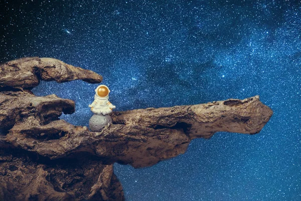 Astronaut wearing white space suit and helmet and meditating while sitting on a rock. Concept of cosmonautics, space travel, freedom, relaxing and peace of mind.