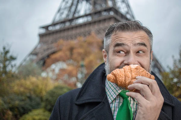 Schöner Mann Anzug Und Mantel Isst Croissant Über Dem Eiffelturm lizenzfreie Stockfotos