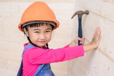 Çocuk mühendis marangoz çekiçle tahta duvarda çalışıyor ve gülümsüyor.