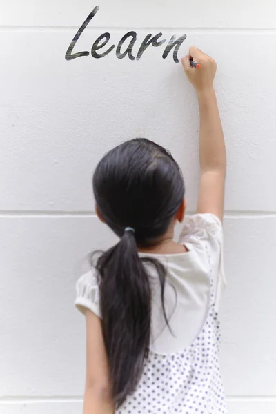 Kid writing learn word on wall with her black pencil