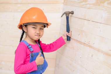 Marangoz olan küçük kız tahta duvarda çekiç ile çalışıyor.