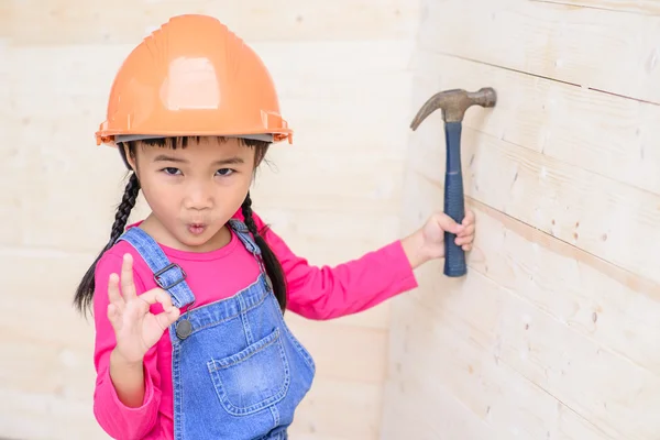 Little girl on carpenter jobs hammer on wood wall and ok sign