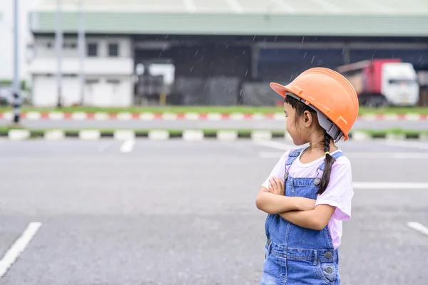 在仓库中心背景下戴橙色头盔的小女孩 运输工作 图库图片