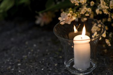 White candle in the glass on floor; Flower in the dark light background 