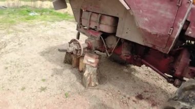 Eski kırmızı bir traktörün tekerlek tamiri ahşap desteklerle kaldırıldı ve sağdan onarıldı..