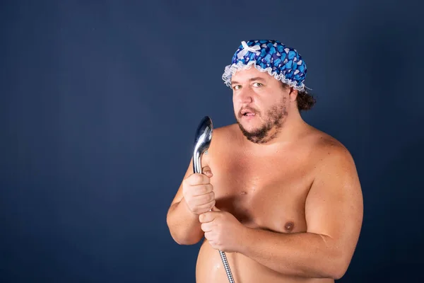 Rolig fet man i blå mössa sjunga i duschen Stockfoto