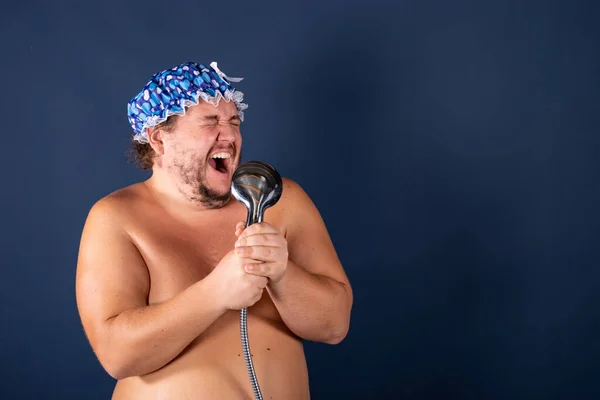 Rolig fet man i blå mössa sjunga i duschen Royaltyfria Stockbilder
