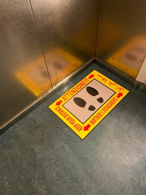 Mesafenizi koruyun: İtalyan bir hastane asansörünün zemininde birden fazla dil işareti var. Sosyal uzaklık. Covid-19 salgını önleme