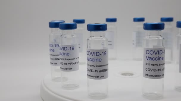 回転ディスプレイ上のCovid 19ワクチンラベルと透明空のガラスのバイアル — ストック動画