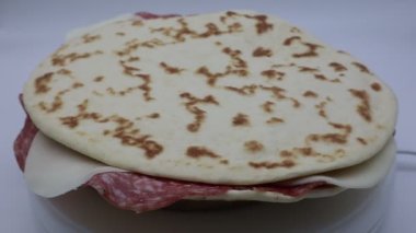 İtalyan Piadina Romagnola. Beyaz arka planda izole edilmiş salamlı ve fontina peynirli düz ekmek.