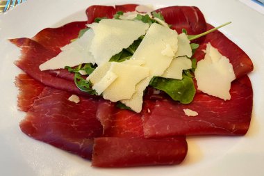 Bir tabak roketli Bresaola ve bir dilim Parmigiano Reggiano peyniri. İtalyan mutfağı.