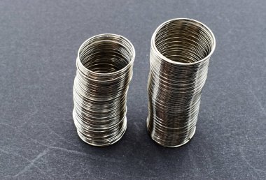 İki uzun, pırıl pırıl gümüş yüzükler dikey olarak koyu gri bir arkaplanda sıralanır..