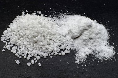 Stüdyonun yakın plan çekimleri beyaz tuz taneciklerinin iki farklı dokusunu koyu bir arkaplan üzerine yerleştirir..