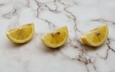 Üç canlı sarı limon, lüks bir beyaz mermer tezgahta simetrik olarak sıralanmıştır. Bu da tazelik ve yemek pişirmeyi işaret eder..
