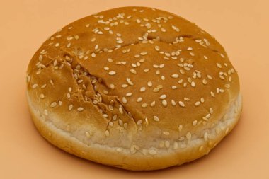 Üzerinde beyaz susam tohumları serpiştirilmiş tek bir altın-kahverengi hamburger ekmeği ticari kullanım için şeftali renkli pürüzsüz bir arka planda duruyor..