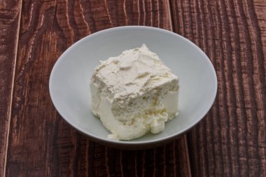 Tahta arka planda bir kasede taze beyaz krem peynir ya da ricotta..