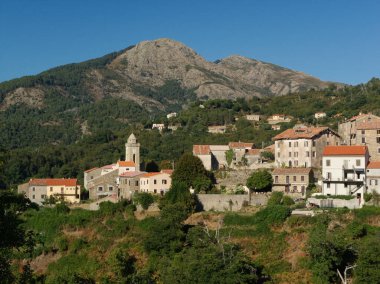 Korsika 'nın mavi gökyüzünün altındaki dağlarda çan kulesi olan küçük bir köye bakın.